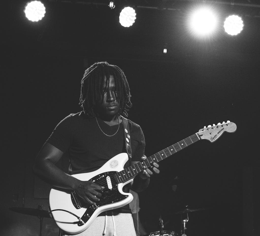 Musician playing electric guitar with stage lights in black and white.